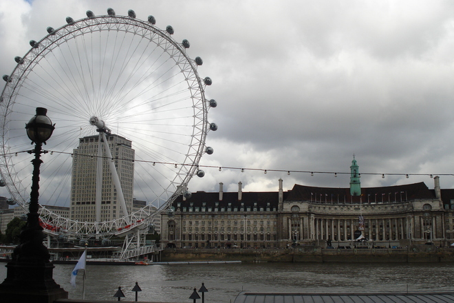 The London Eye stands tall over the Thames River on a cloudy London day. 